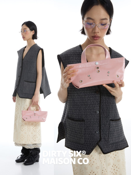Fashion model wearing a textured black vest and holding a pink handbag on a white background