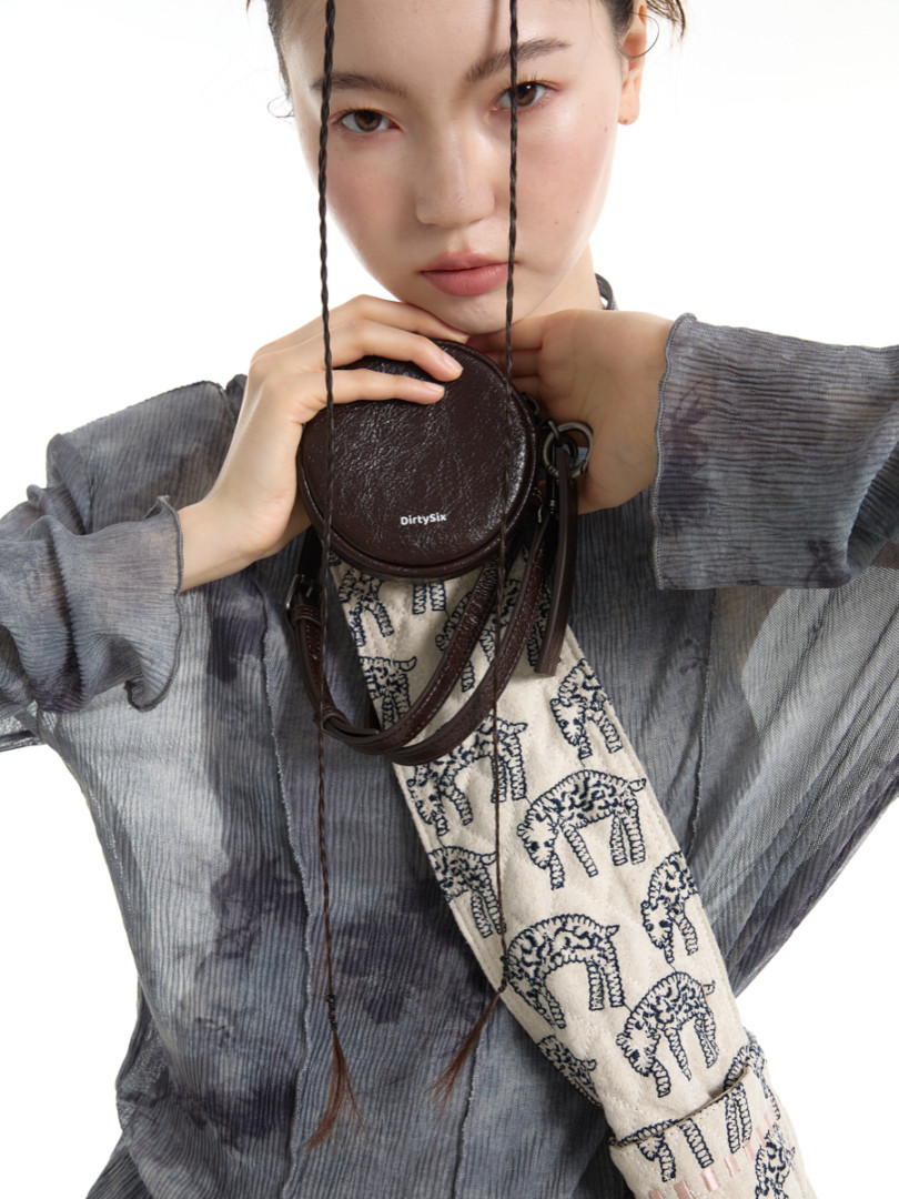 Model holding a small round leather crossbody bag