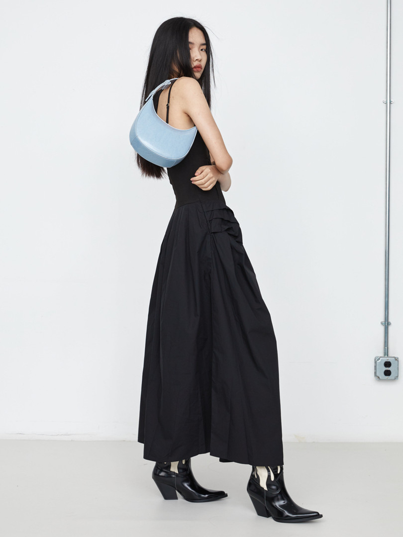 Model wearing a black sleeveless maxi dress with black boots and a light blue shoulder bag
