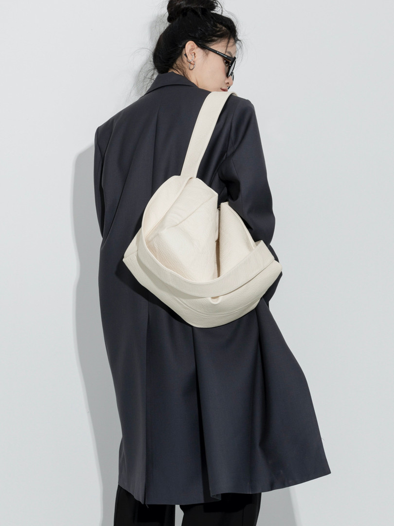 Model wearing a black long coat with a cream shoulder bag
