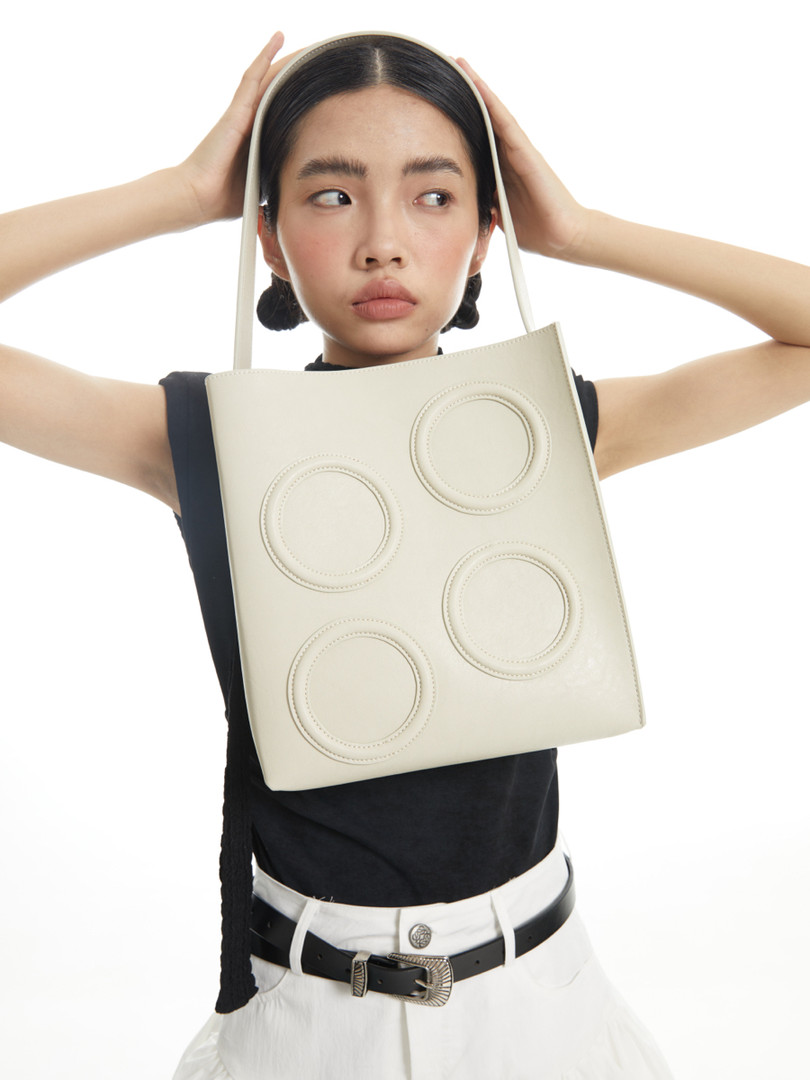 Cream tote handbag worn by a model against a white background