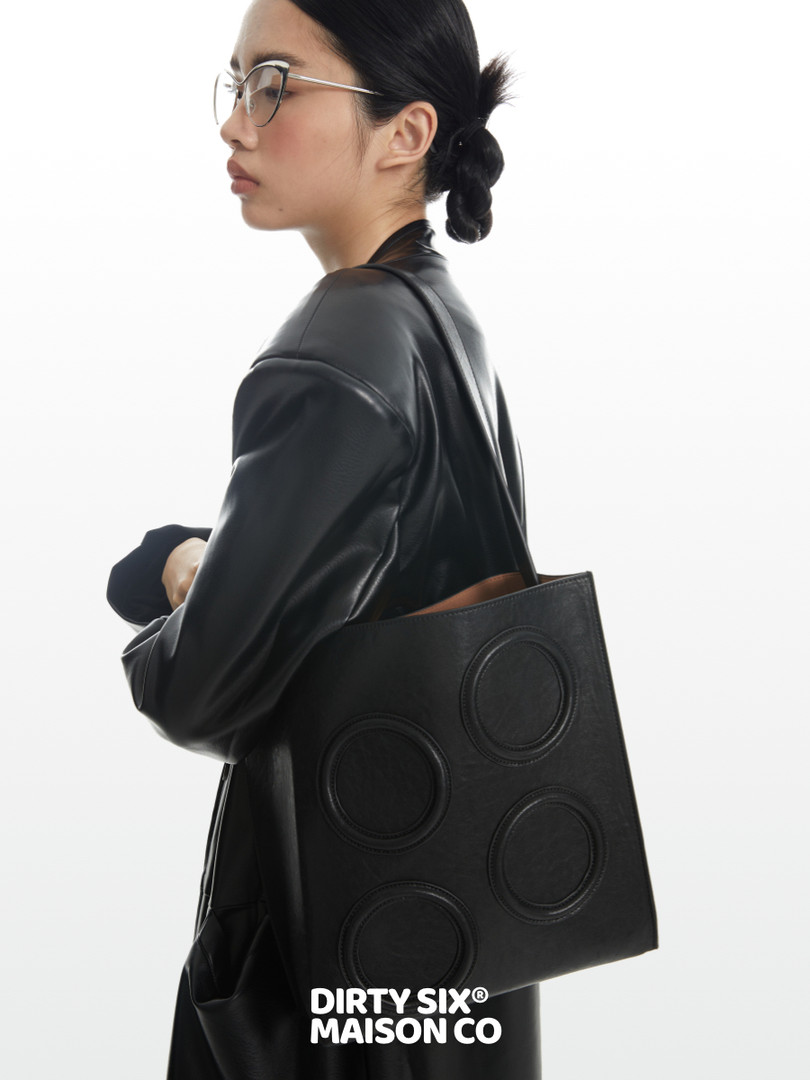 Model wearing a black coat and carrying a black tote bag