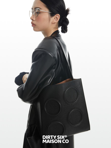 Model wearing a black coat and carrying a black tote bag