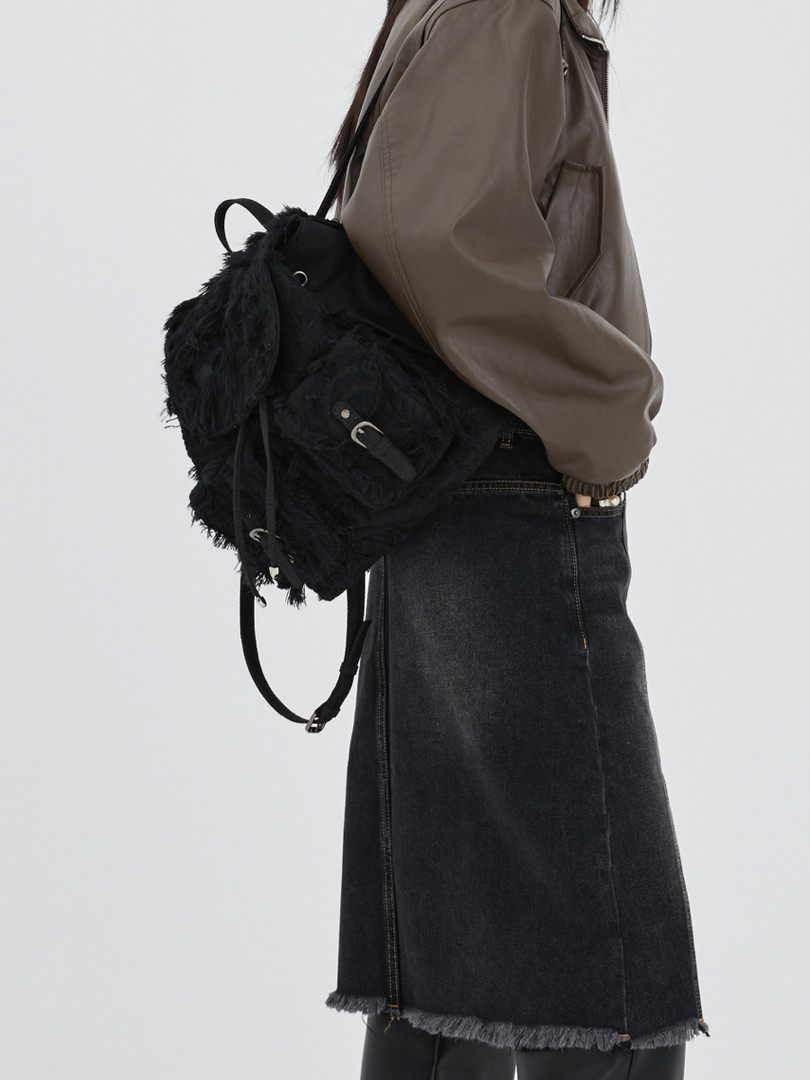 Black fuzzy backpack worn by a model with a brown jacket and black denim skirt