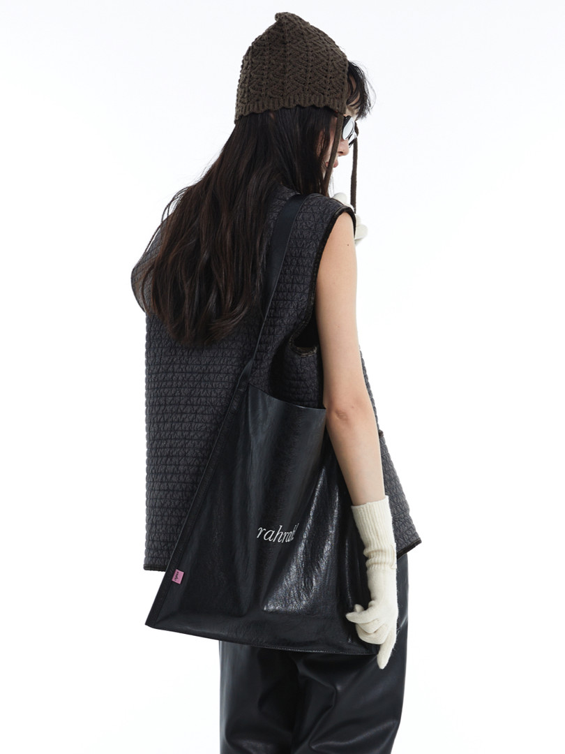 Model wearing a black textured outfit and carrying a black tote bag
