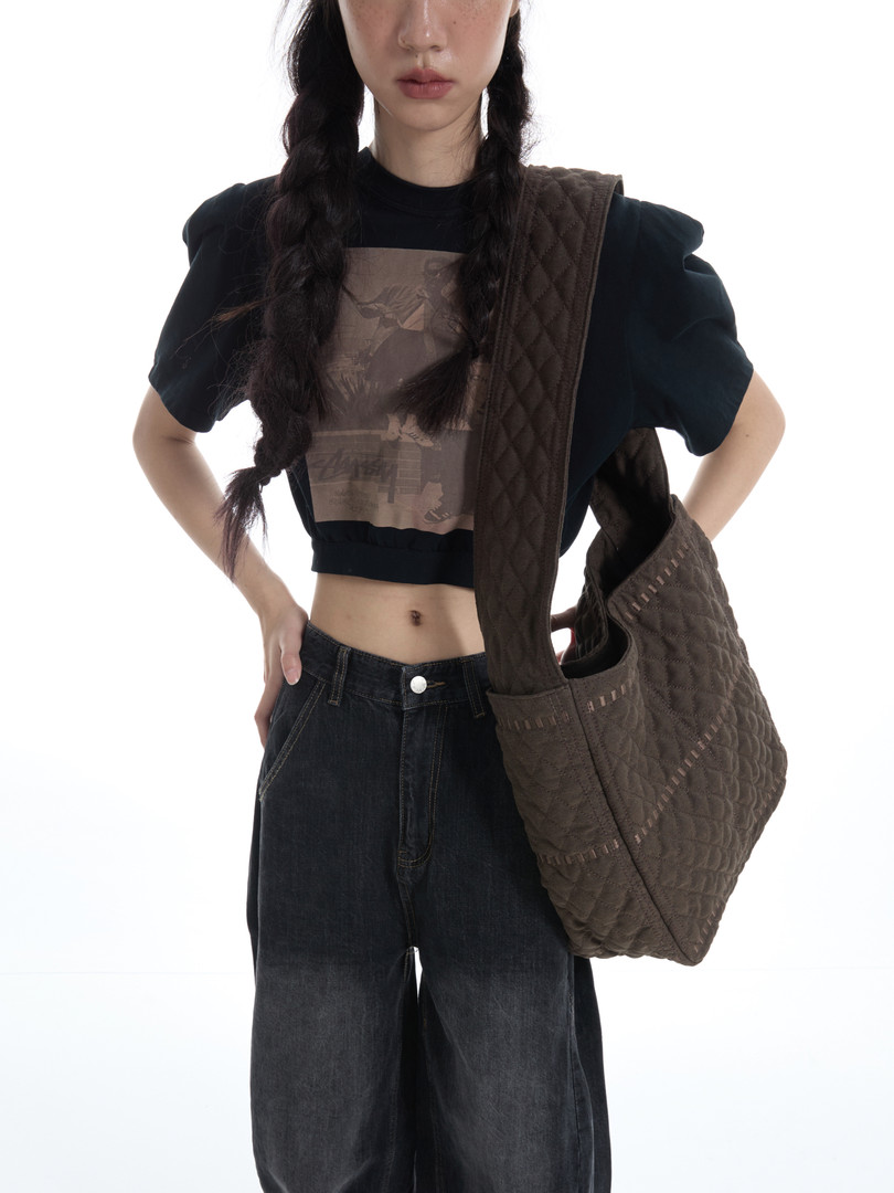 Model wearing a black crop top, dark jeans, and a large quilted brown shoulder bag