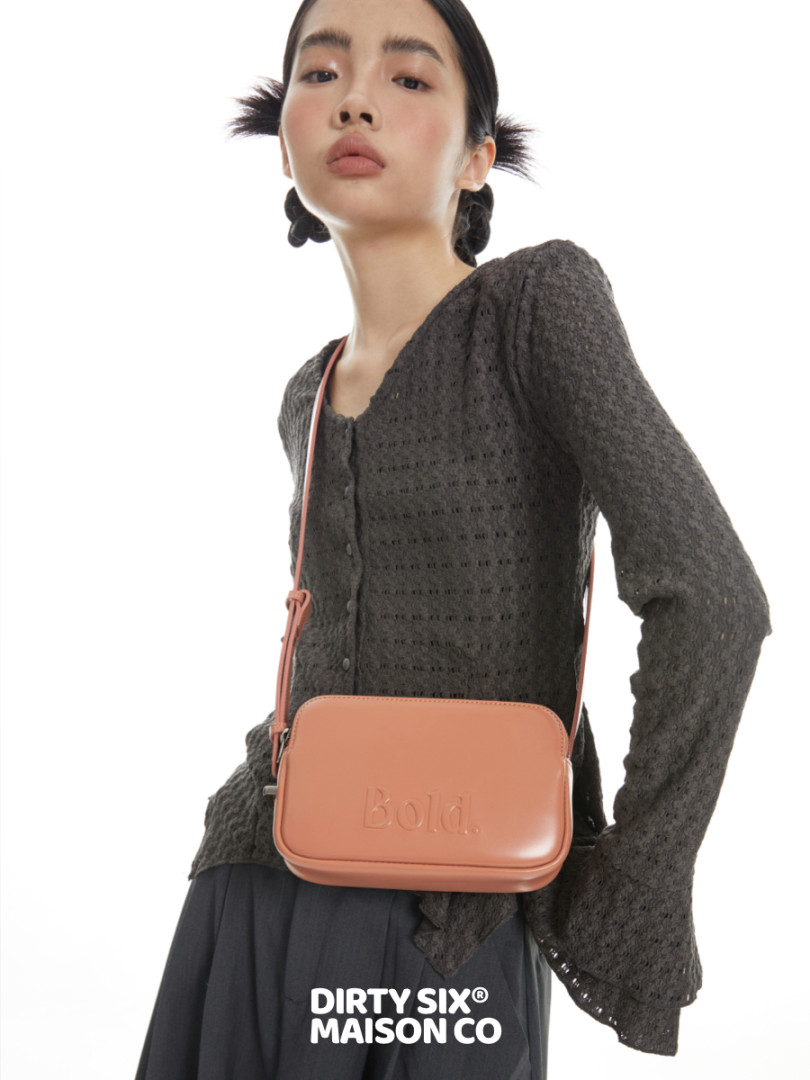 Model wearing a dark textured top with a peach crossbody bag