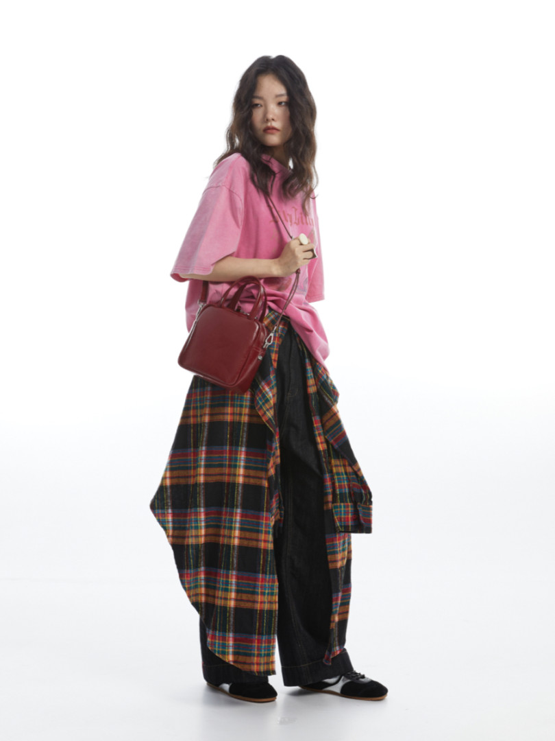 Model wearing an oversized pink T-shirt with plaid layered bottoms and a burgundy handbag