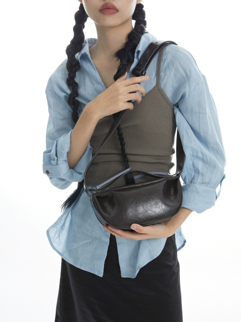 Black leather shoulder bag worn by a model with a light blue shirt