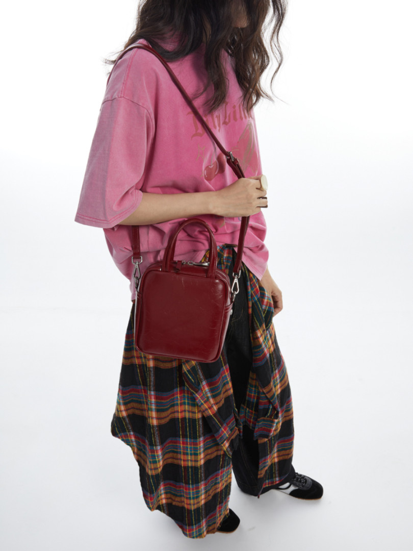 Model wearing a burgundy crossbody bag with a pink oversized tee and plaid pants