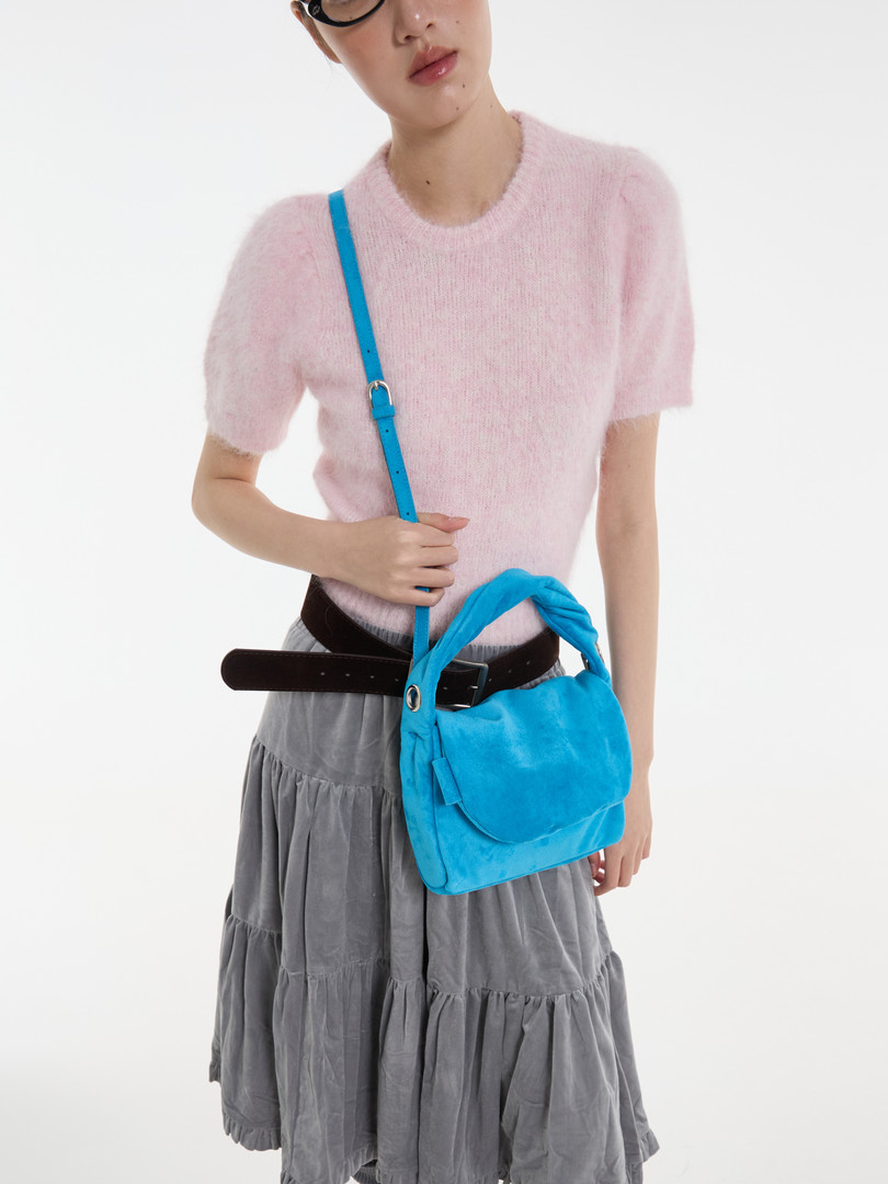 Model wearing a pink short-sleeve fuzzy top with a bright blue shoulder bag