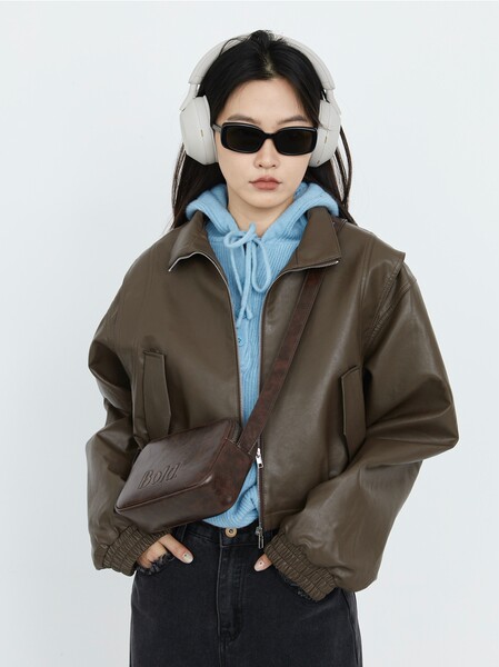 Model wearing a brown leather jacket over a blue hoodie with a crossbody bag