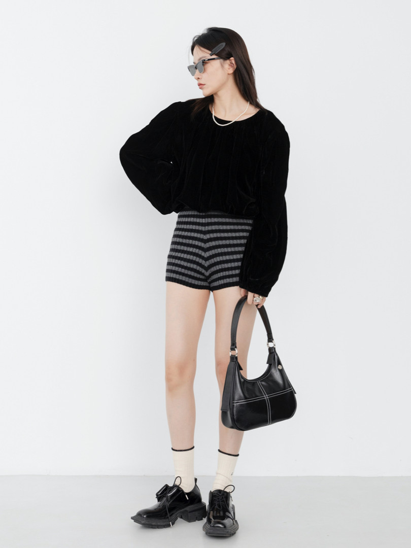 Model wearing a black top, striped shorts, and carrying a black handbag
