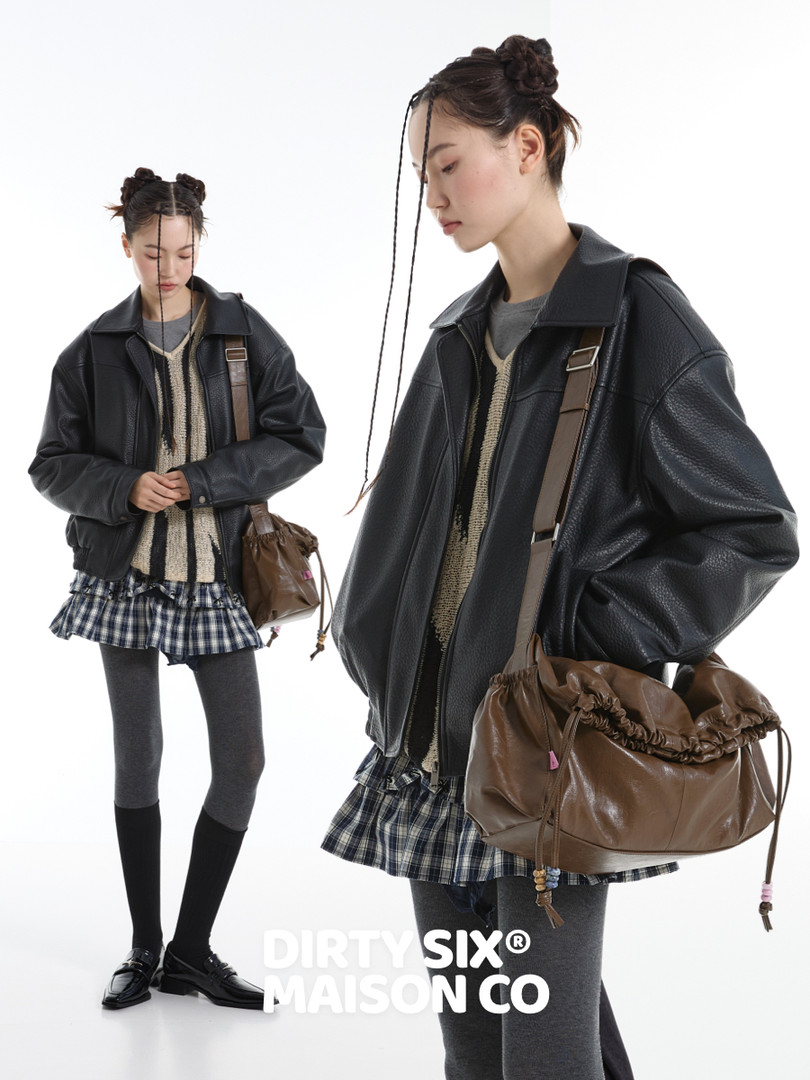 Model wearing a black leather jacket with a brown shoulder bag and plaid skirt outfit