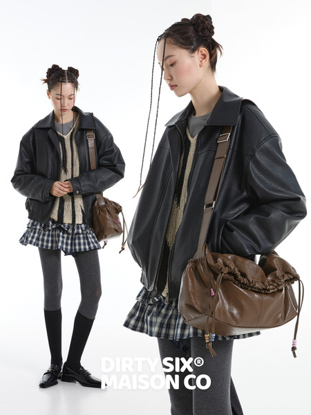Model wearing a black leather jacket with a brown shoulder bag and plaid skirt outfit