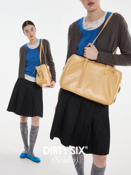 Fashion model wearing a blue top, dark cardigan and skirt, carrying a tan leather shoulder bag