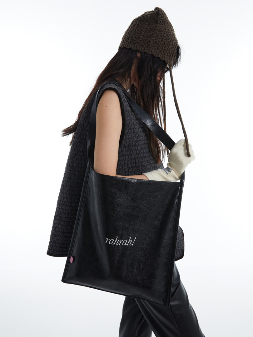 Black leather tote bag worn by a model on a white background