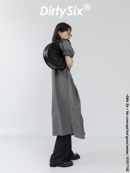 Model wearing a gray dress with black pants and a black circular backpack