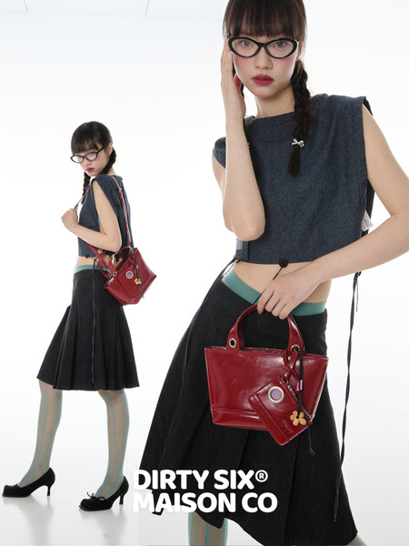 Fashion model wearing a dark sleeveless top, black pleated skirt, and red handbag