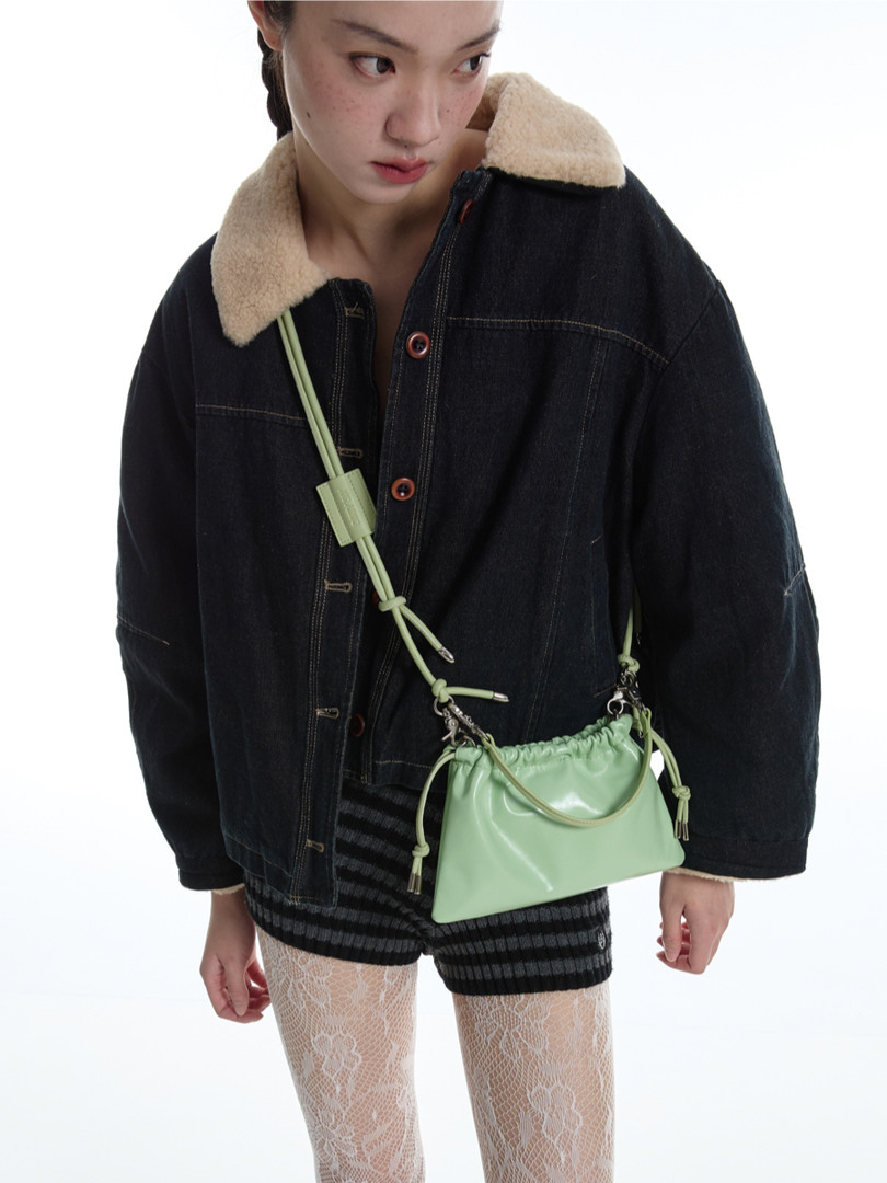Model wearing a black denim jacket with shearling collar and a mint green crossbody bag