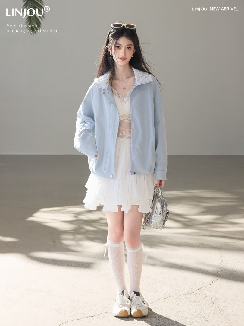 Model wearing a light blue jacket over a white dress with sneakers and a silver handbag