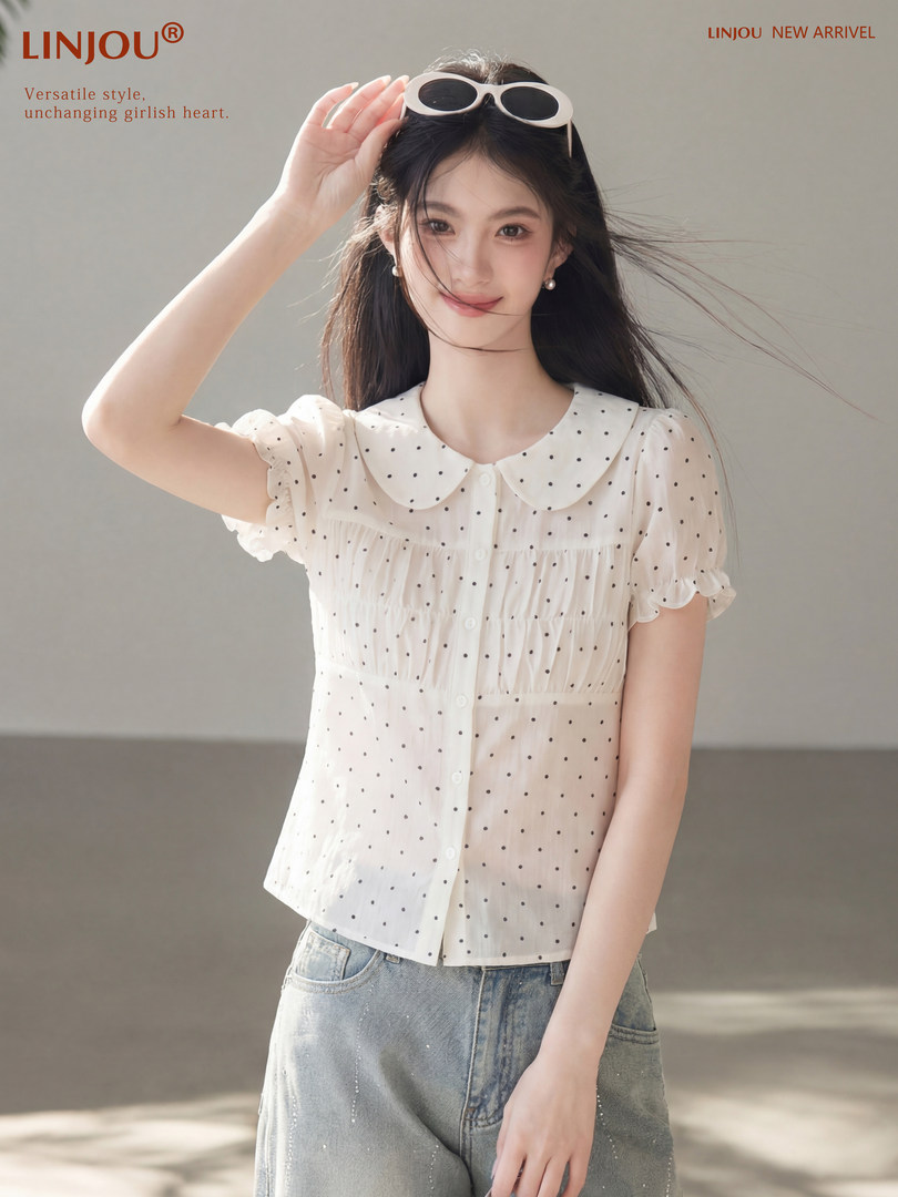 Model wearing a white polka dot short-sleeve blouse with a Peter Pan collar and jeans