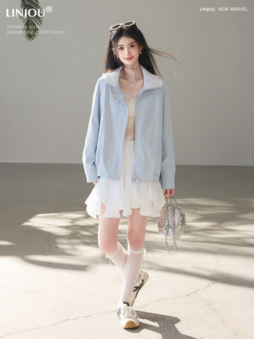 Model wearing a light blue jacket and white skirt outfit with a small handbag