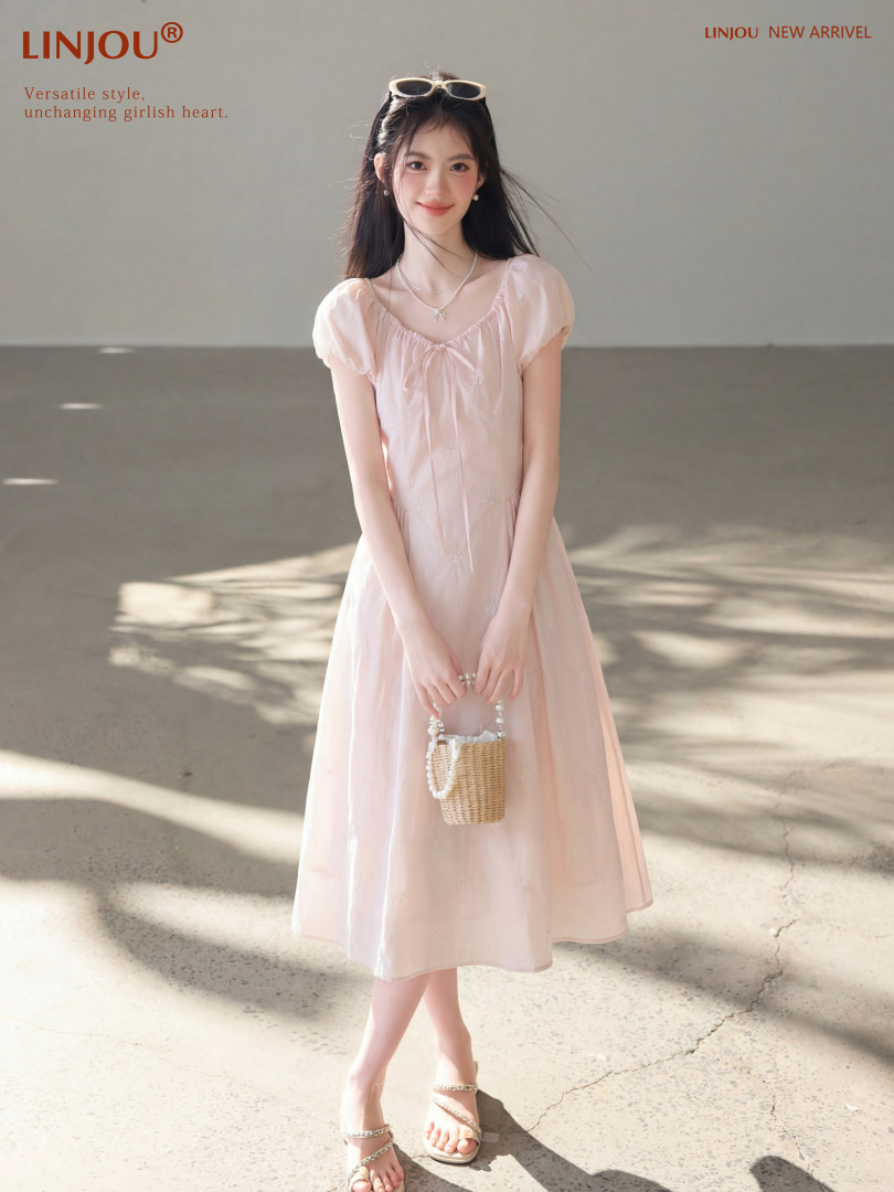 Model wearing a light pink puff-sleeve dress with a small woven handbag