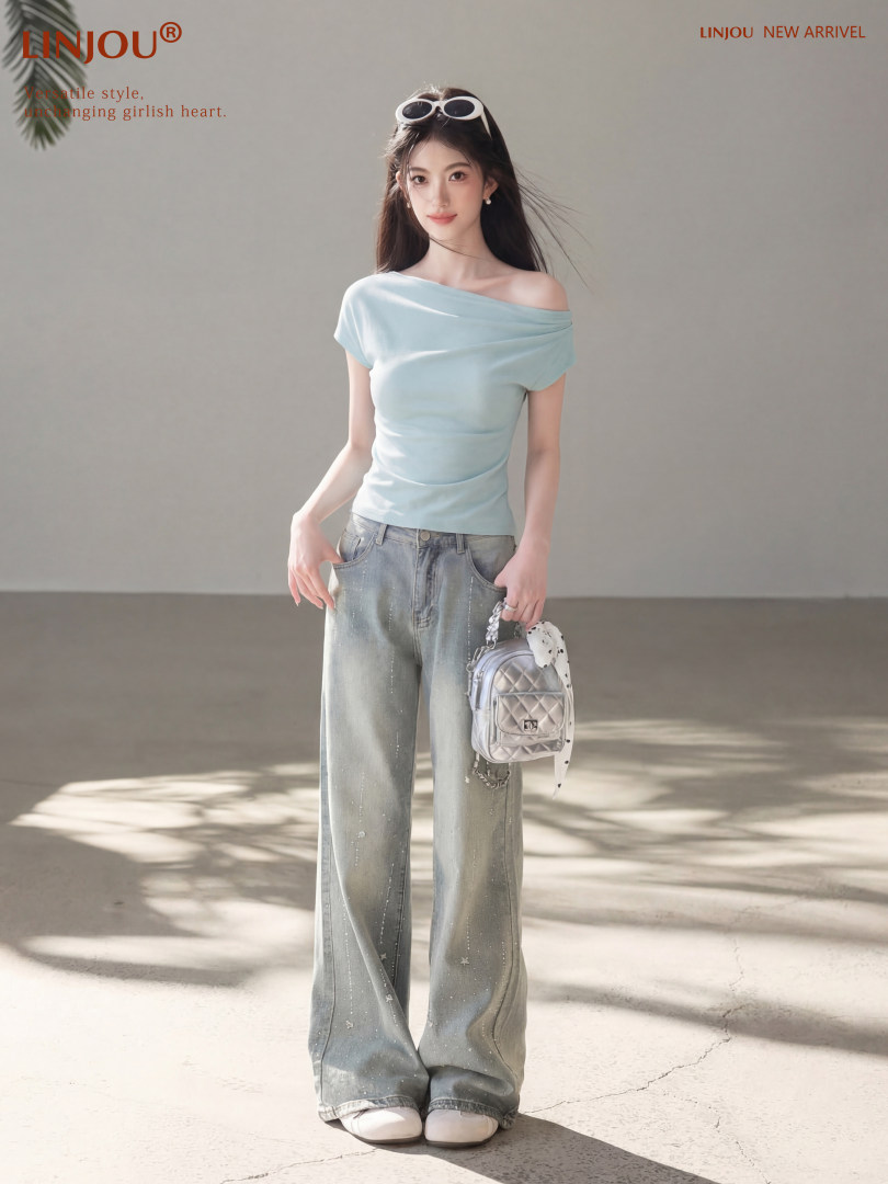 Model wearing a light blue off-shoulder top with wide-leg jeans and a small metallic backpack