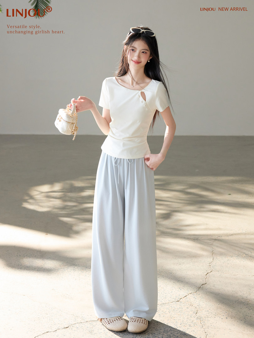 Model wearing a white short-sleeve top and light blue wide-leg pants with a small handbag