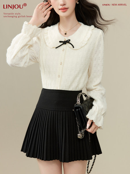 Model wearing a white ruffled blouse with a black pleated skirt and black handbag