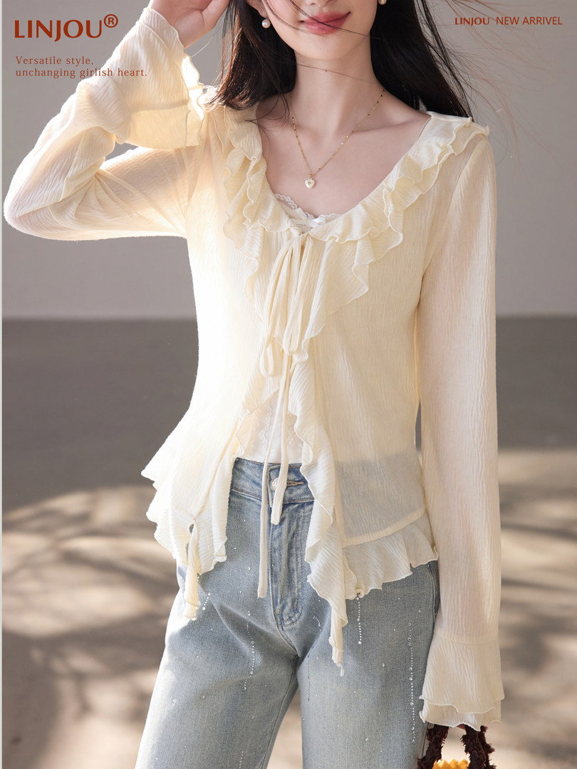 Model wearing a cream ruffled long-sleeve sheer blouse with jeans