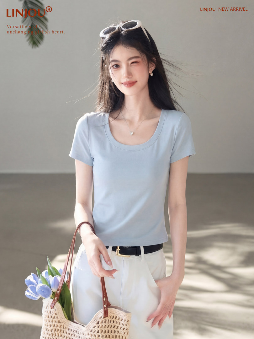 Woman wearing a light blue short-sleeve scoop-neck top with white pants and a woven bag
