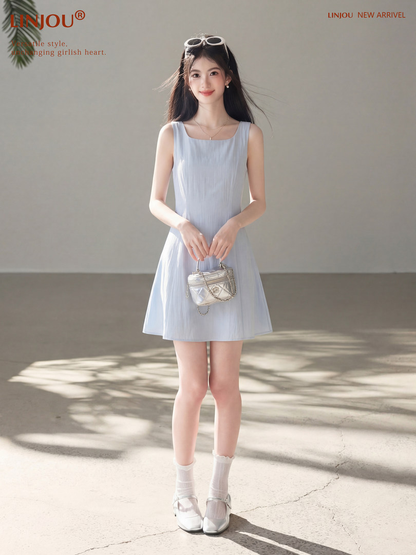 Model wearing a light blue sleeveless dress and white shoes while holding a small handbag