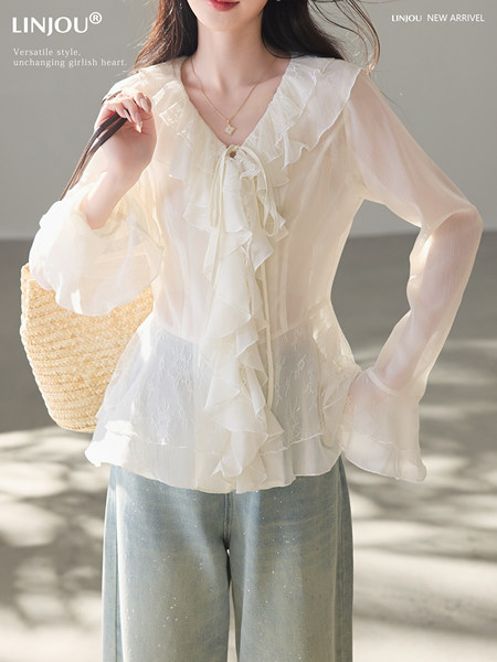 Model wearing a white ruffled sheer blouse with light blue jeans