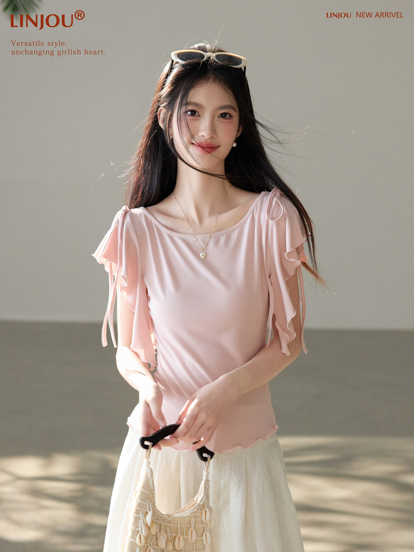 Model wearing a light pink ruffle-sleeve blouse with a cream skirt