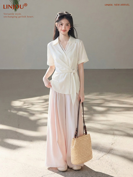 Model wearing a white short-sleeve wrap blouse with a long pink skirt and straw tote bag