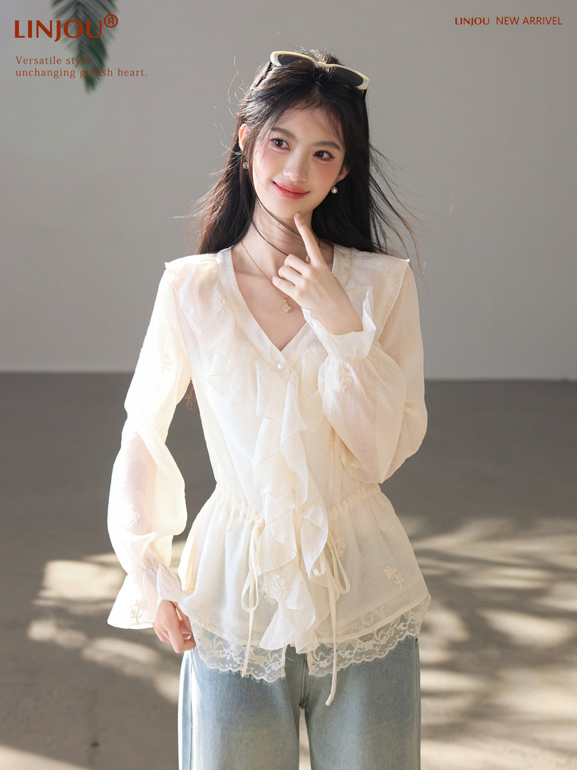 Model wearing a white sheer ruffled blouse with lace trim and light blue jeans