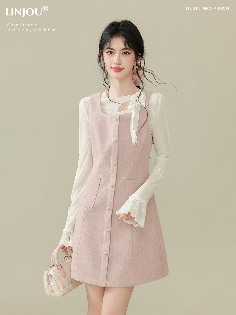 Pink pinafore dress layered over a white blouse, worn by a model with a handbag.