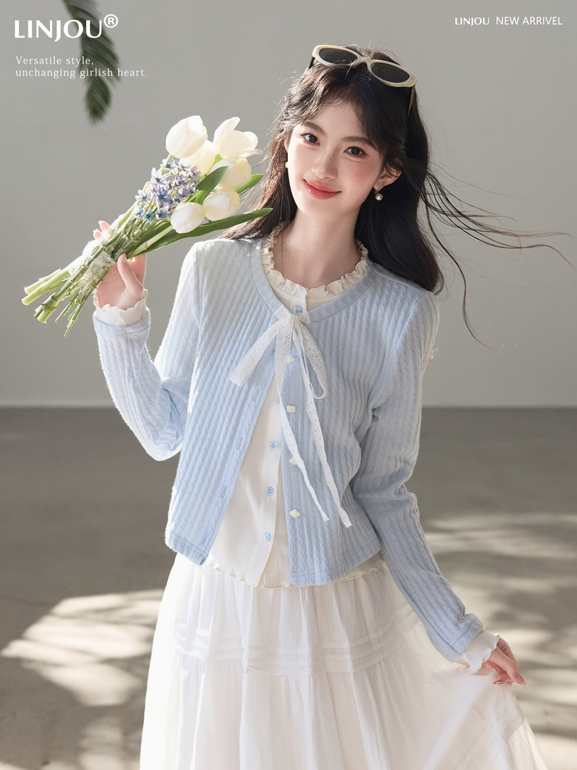 Model wearing a light blue cardigan over a white dress, holding flowers