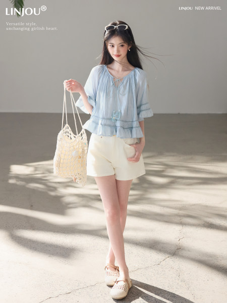 Model wearing a light blue ruffled blouse with white shorts and a woven tote bag