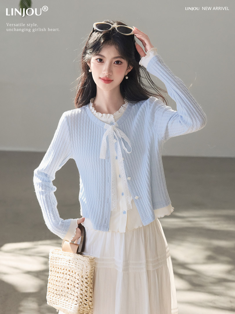 Model wearing a light blue cardigan over a white dress with a woven bag