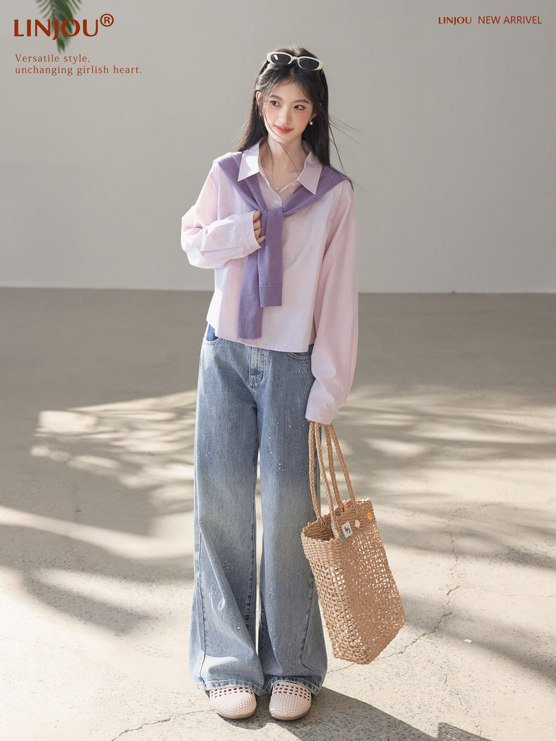 Model wearing a pastel pink blouse with a purple sweater draped over the shoulders and wide-leg jeans, carrying a woven tote bag