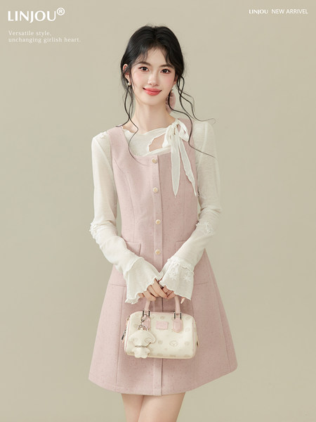 Model wearing a pink sleeveless dress over a white blouse and holding a small handbag