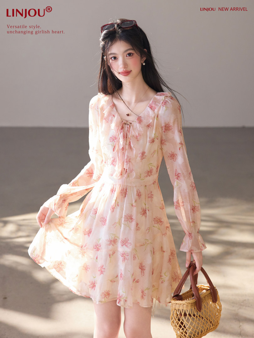 Model wearing a light pink floral long-sleeve dress with a small woven handbag