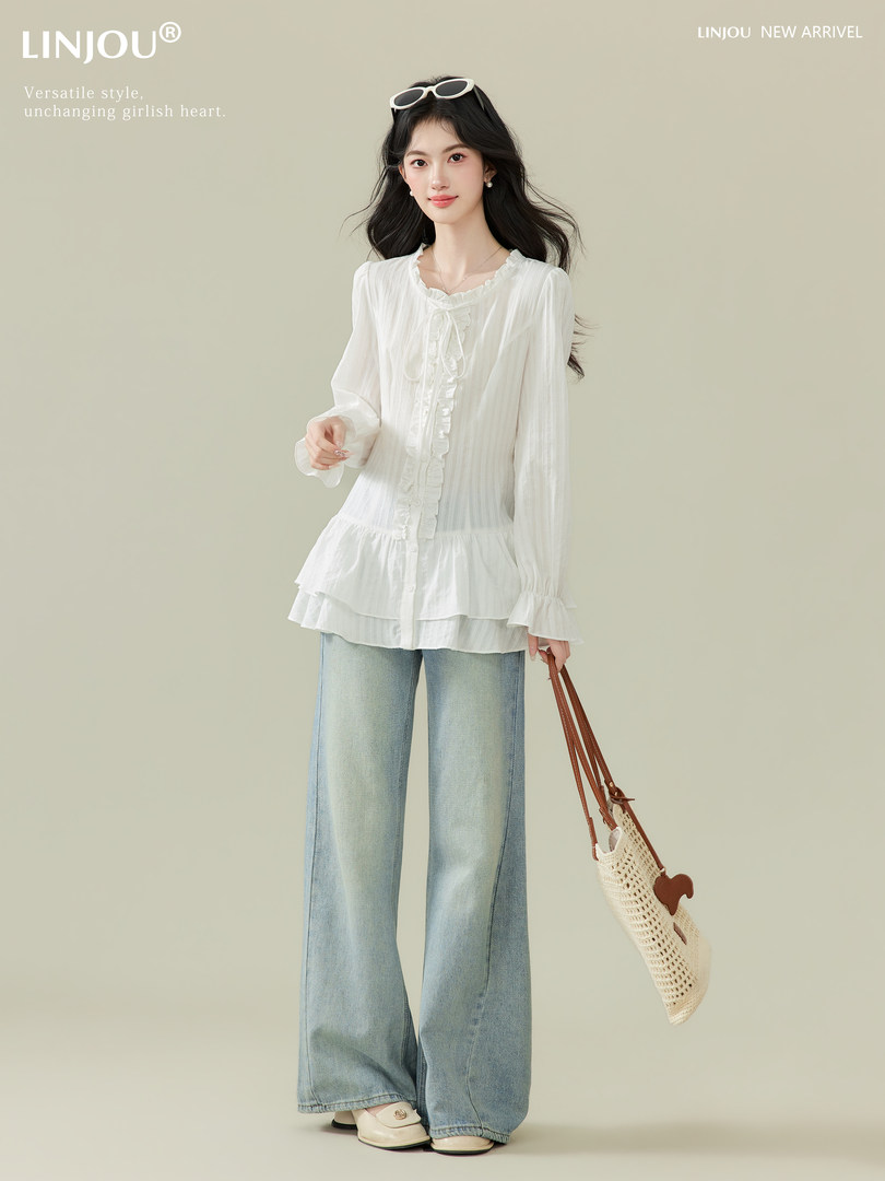 Model wearing a white ruffled blouse with wide-leg light blue jeans and a woven shoulder bag