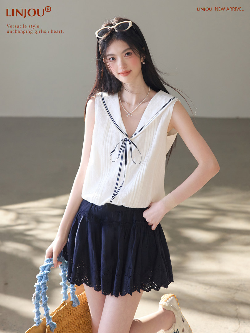 Model wearing a white sailor-style sleeveless top and navy skirt outdoors