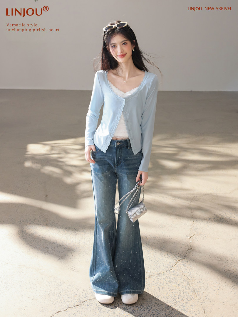 Woman wearing a light blue cardigan over a white lace top with wide-leg jeans and a small handbag