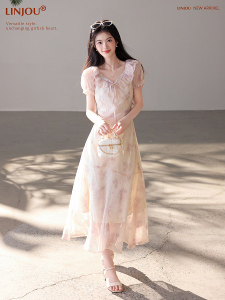 Woman wearing a light pink floral ruffled dress with a small white handbag