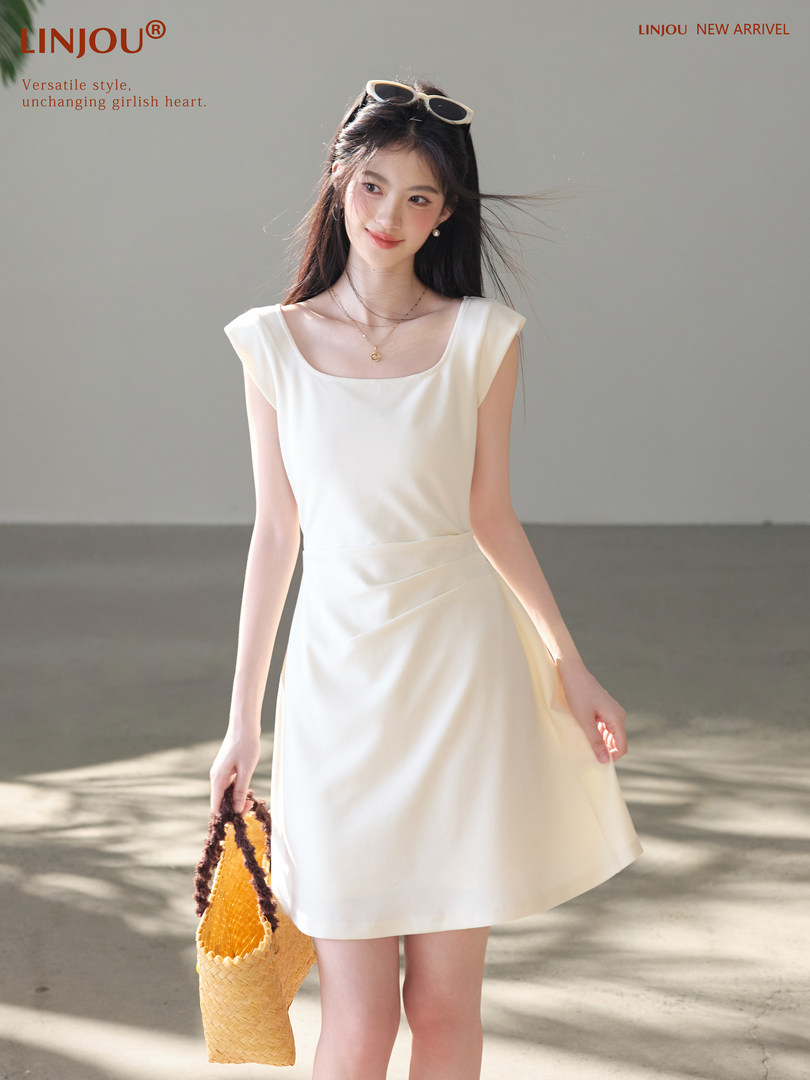 White sleeveless dress worn by a model holding a woven straw bag